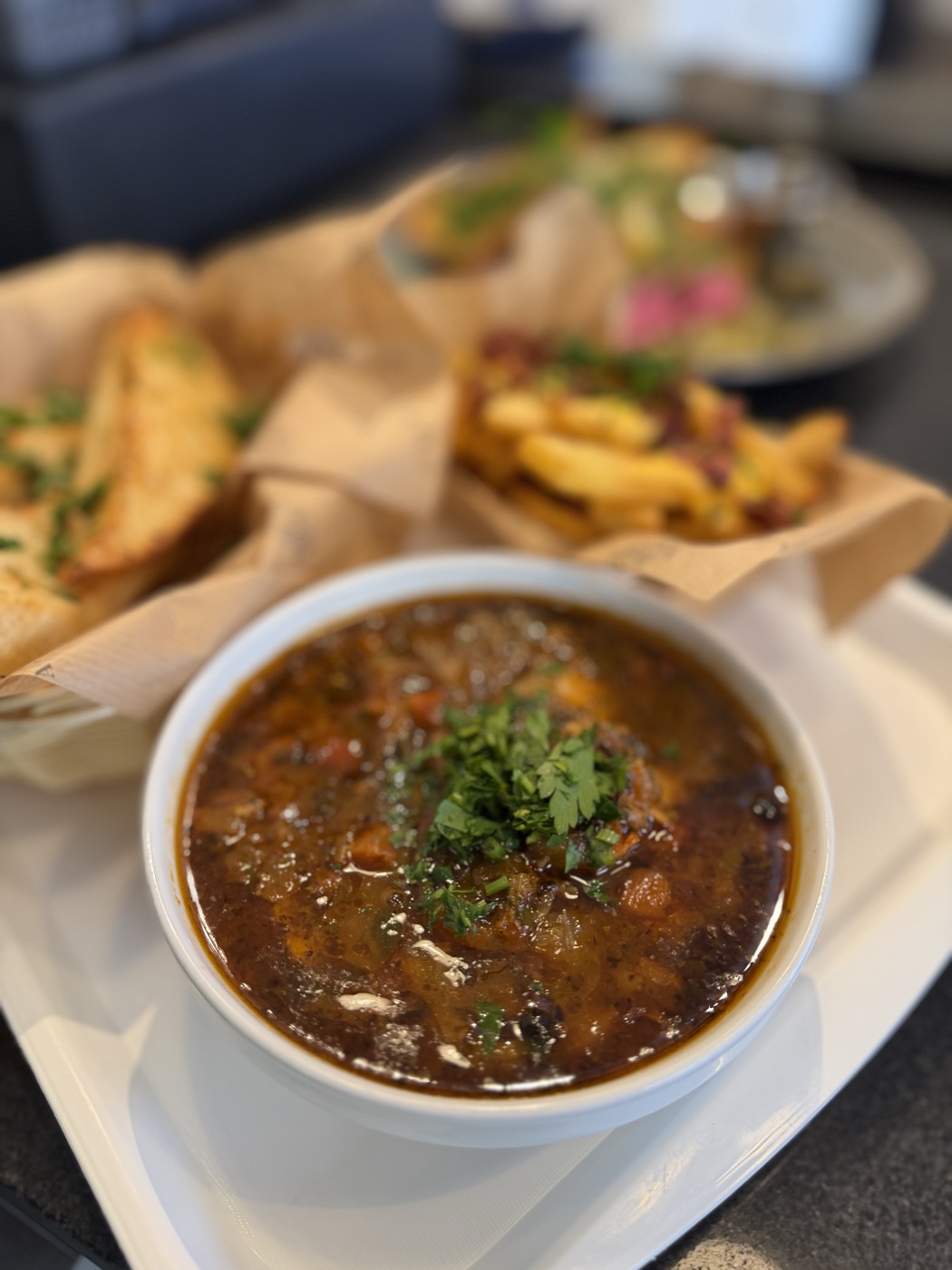 Węgierska zupa rybna Halászlé — gęsty wywar z natką pietruszki, podana w białej misce z grzankami i frytkami w tle