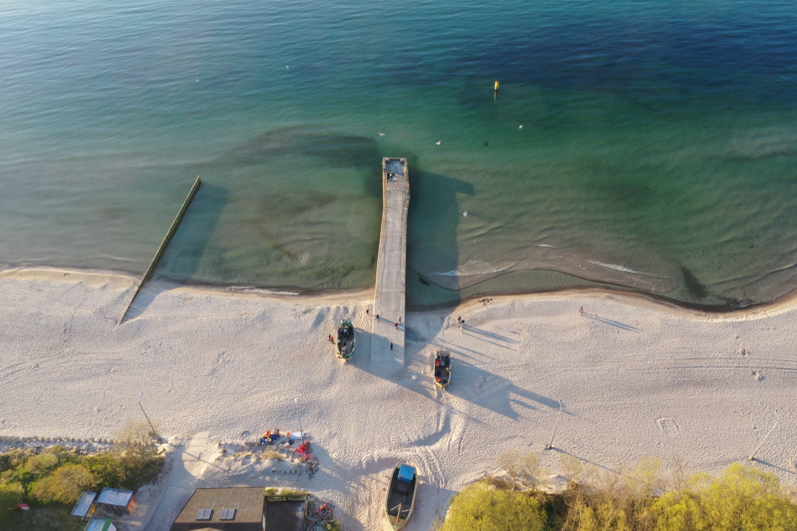 Wybrzeże Niechorza z drona — falochron, piana morska, klif w oddali